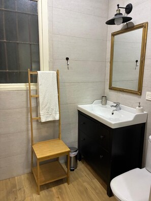 A bathroom with a wooden stool, a white sink, a black cabinet, a toilet, and a mirror with a gold frame. - Vrbo Property (Donostia / San Sebastián)