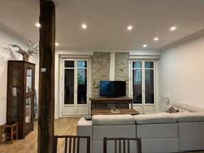 A living room with a sofa, television, and a stone wall. - Vrbo Property (Donostia / San Sebastián)