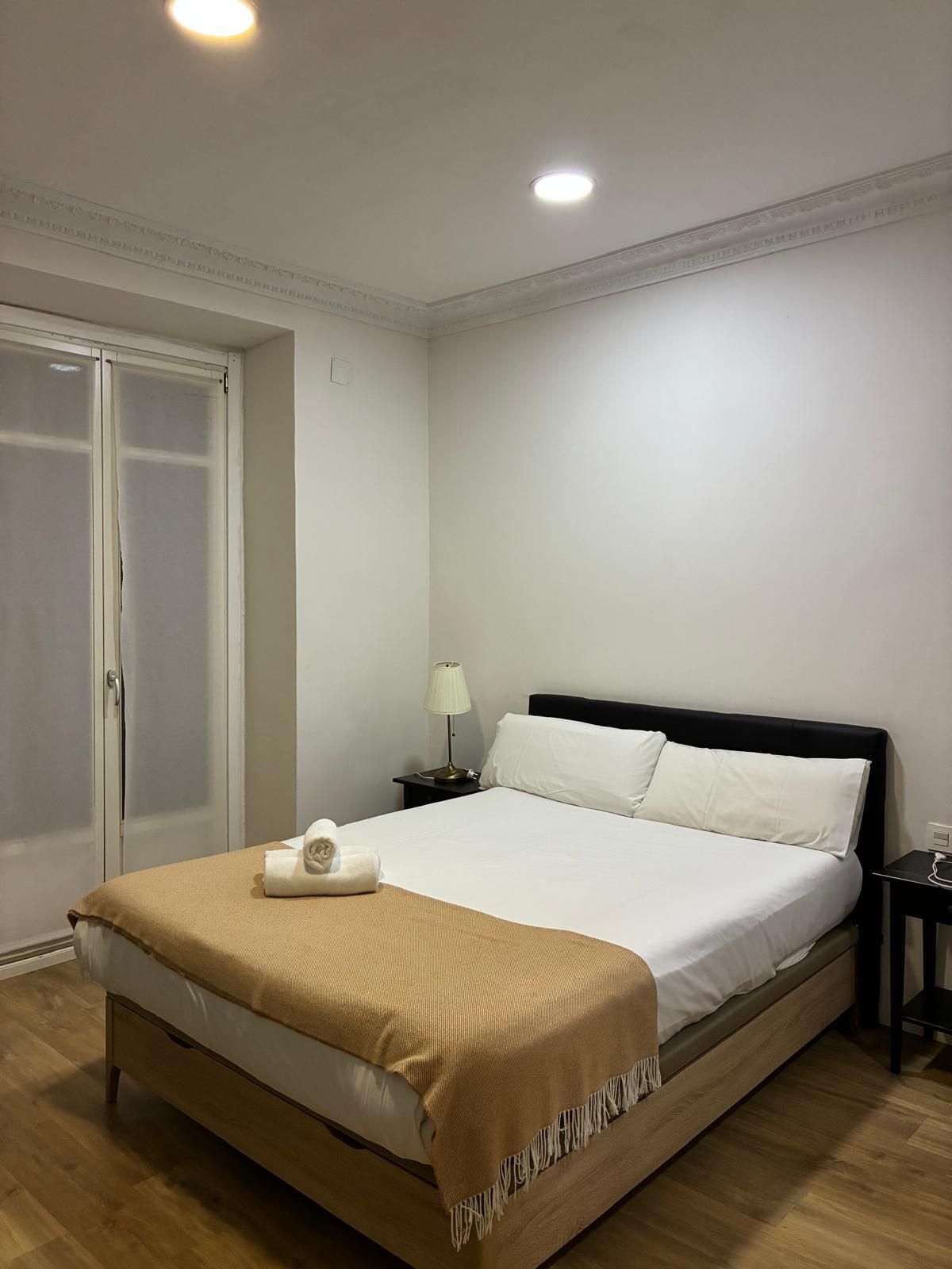 Una habitación de hotel con cama, mesita de noche, lámpara y puerta.