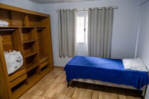 Ein Schlafzimmer mit einem Einzelbett, einem Holzschrank und einem Fenster mit Vorhängen.
