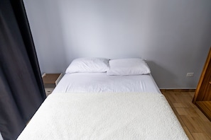 Ein Einzelbett mit weißer Bettwäsche in einem Zimmer mit hellen Wänden und Holzboden.