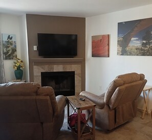 A living room with a flat-screen TV mounted above a fireplace, two brown leather sofas, a small wooden coffee table, and a painting on the wall. - Peaceful Laughlin Oasis - First Floor- No Stairs (Laughlin)