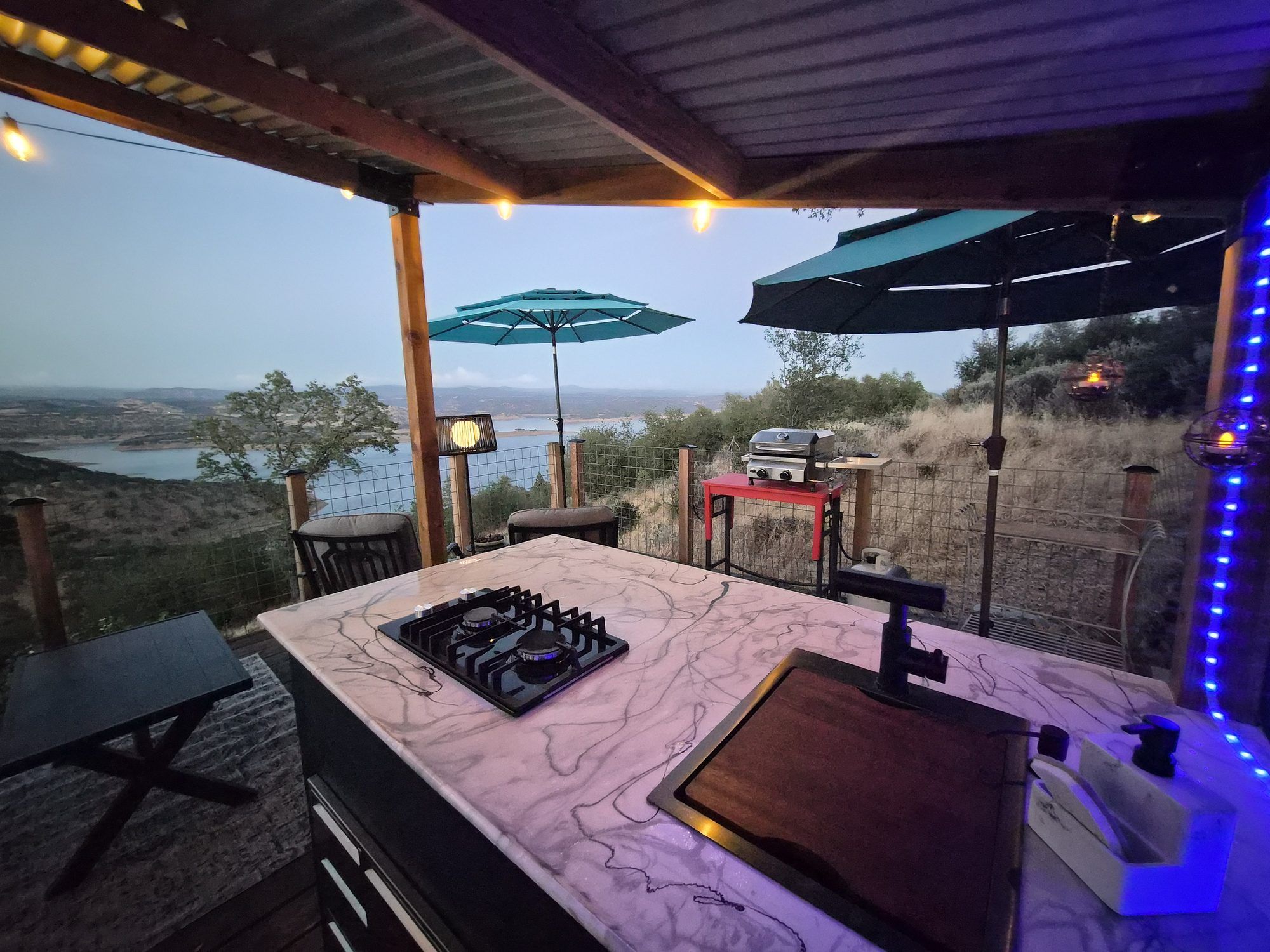 An outdoor kitchen with a gas stove, a grill, and a view of the landscape.