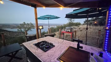 An outdoor kitchen with a gas stove, a grill, and a view of the landscape.