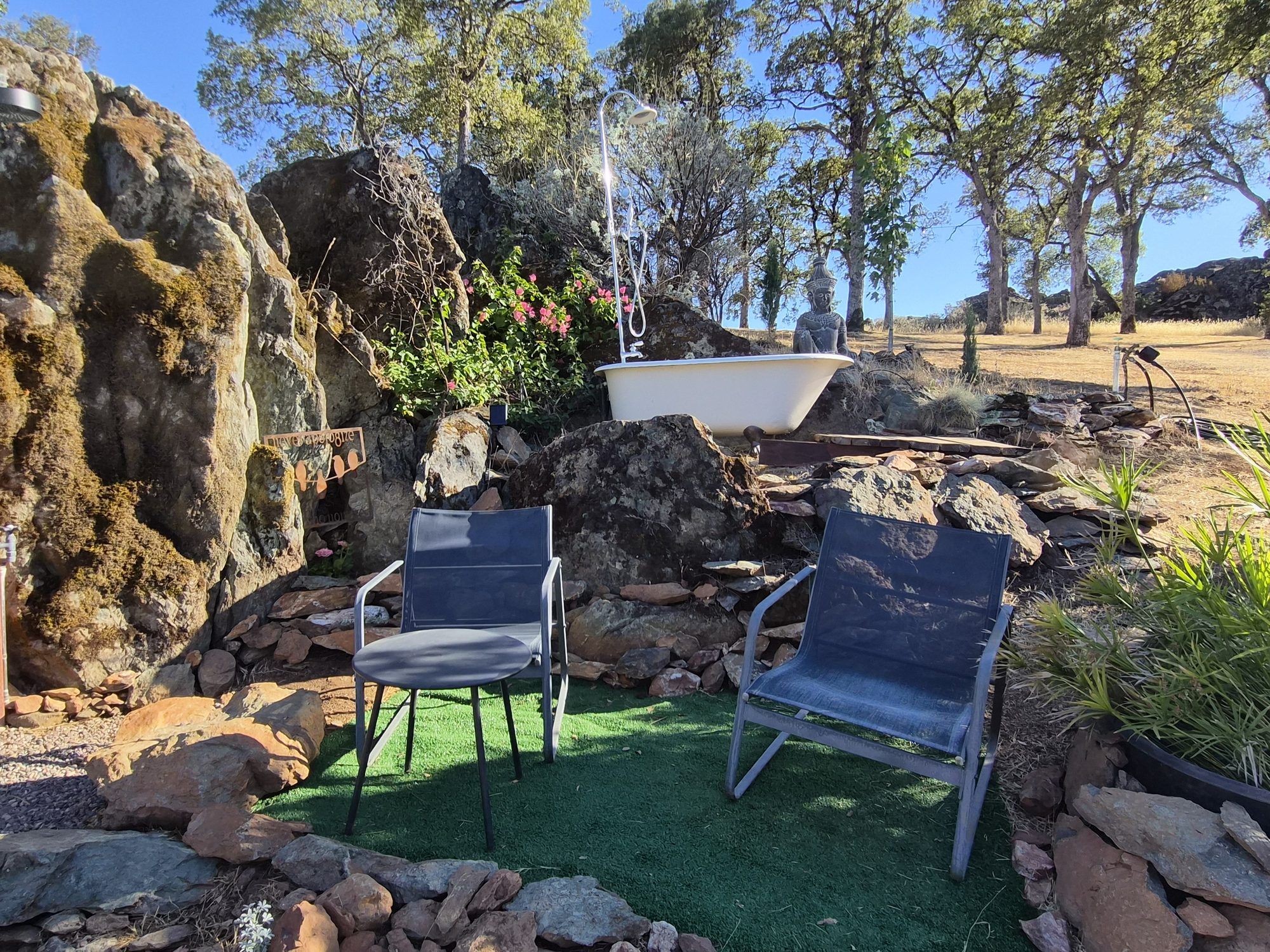 A rock garden with two chairs, a white basin, and a Buddha statue.