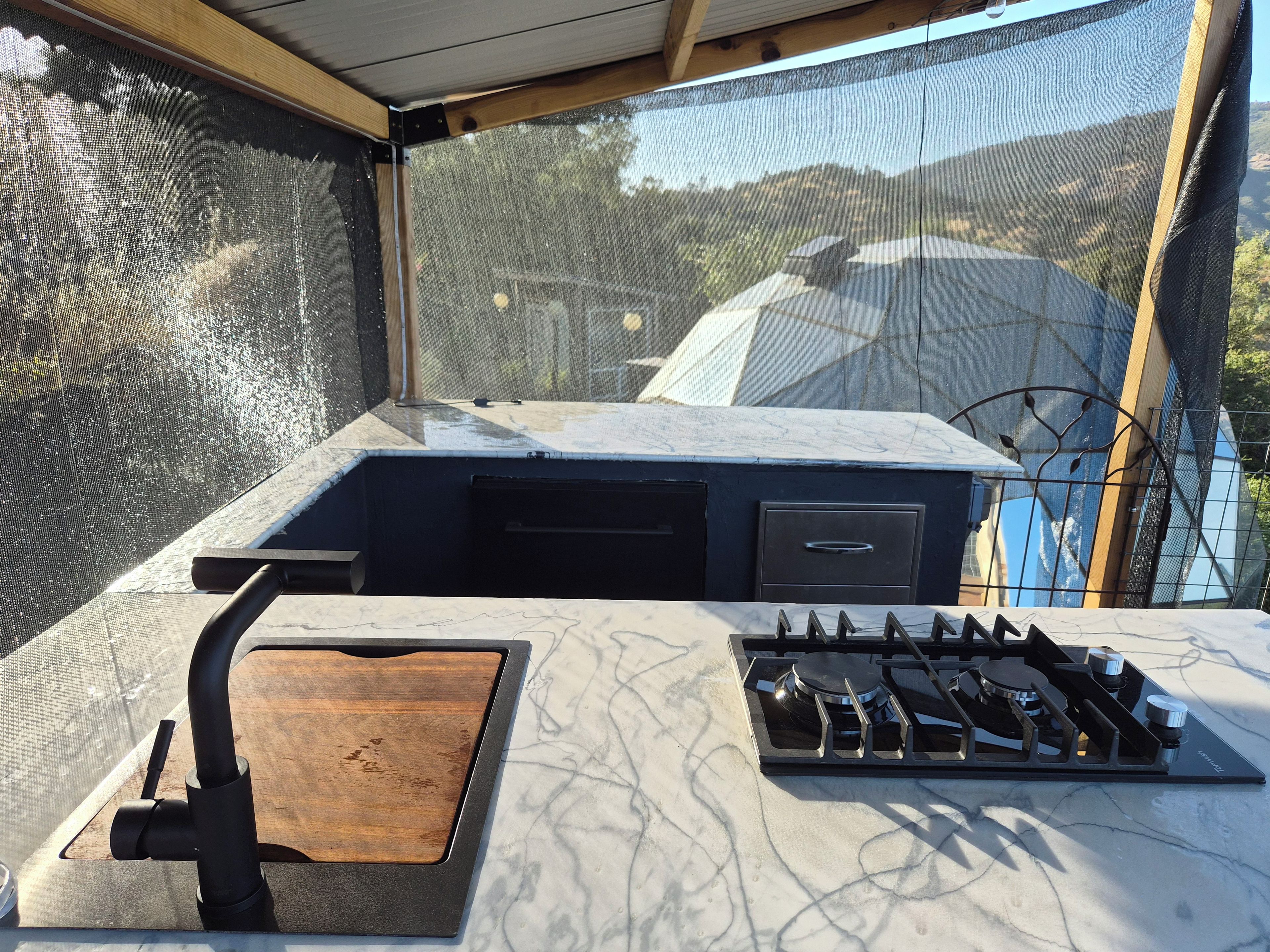 A kitchen with a gas stove, a wooden cutting board, and a view through a window.
