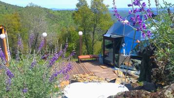 A wooden deck with a bench, a glass-enclosed structure, and a hot tub.