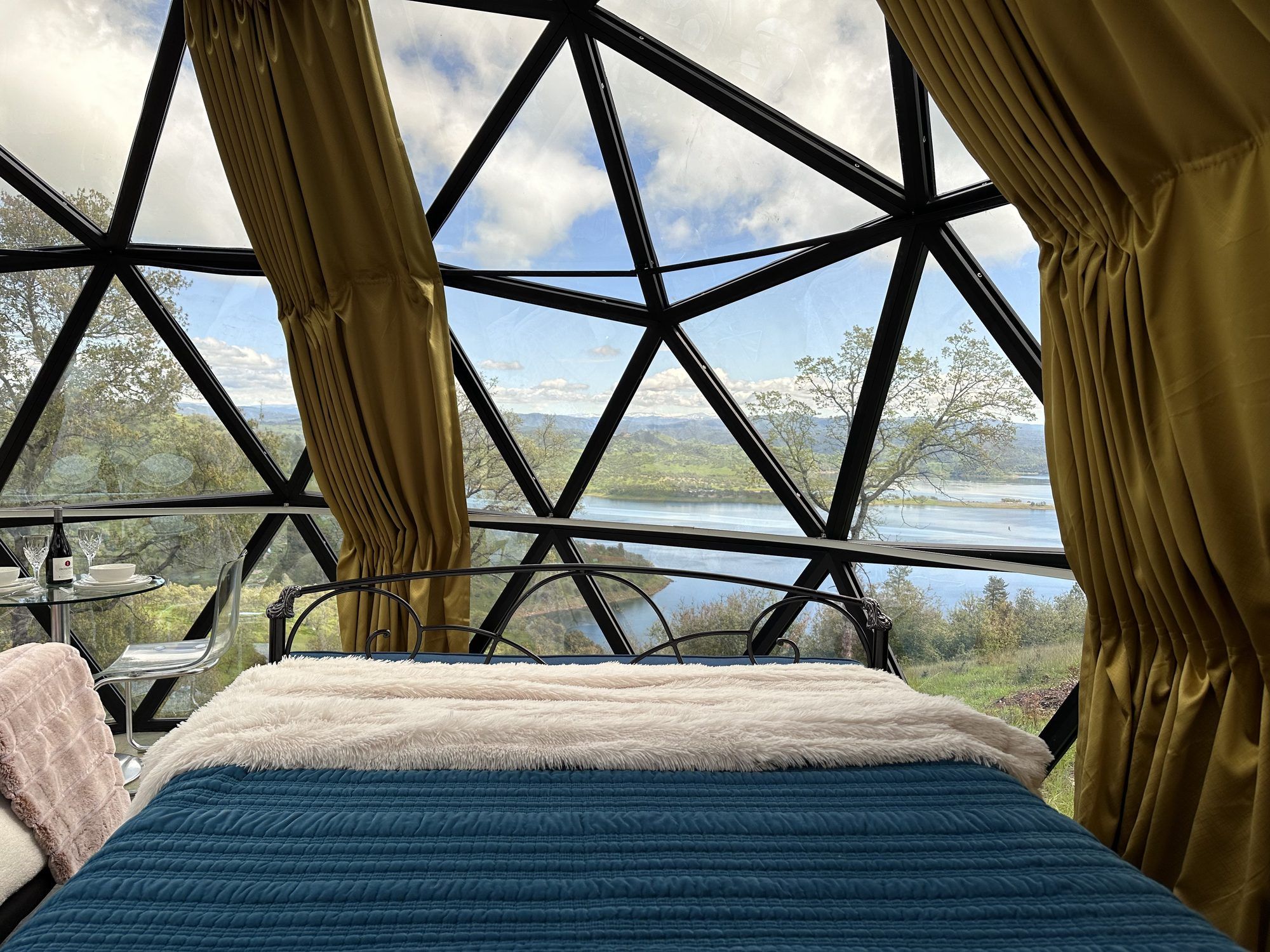 A room with a bed, a table with a bottle, and curtains.