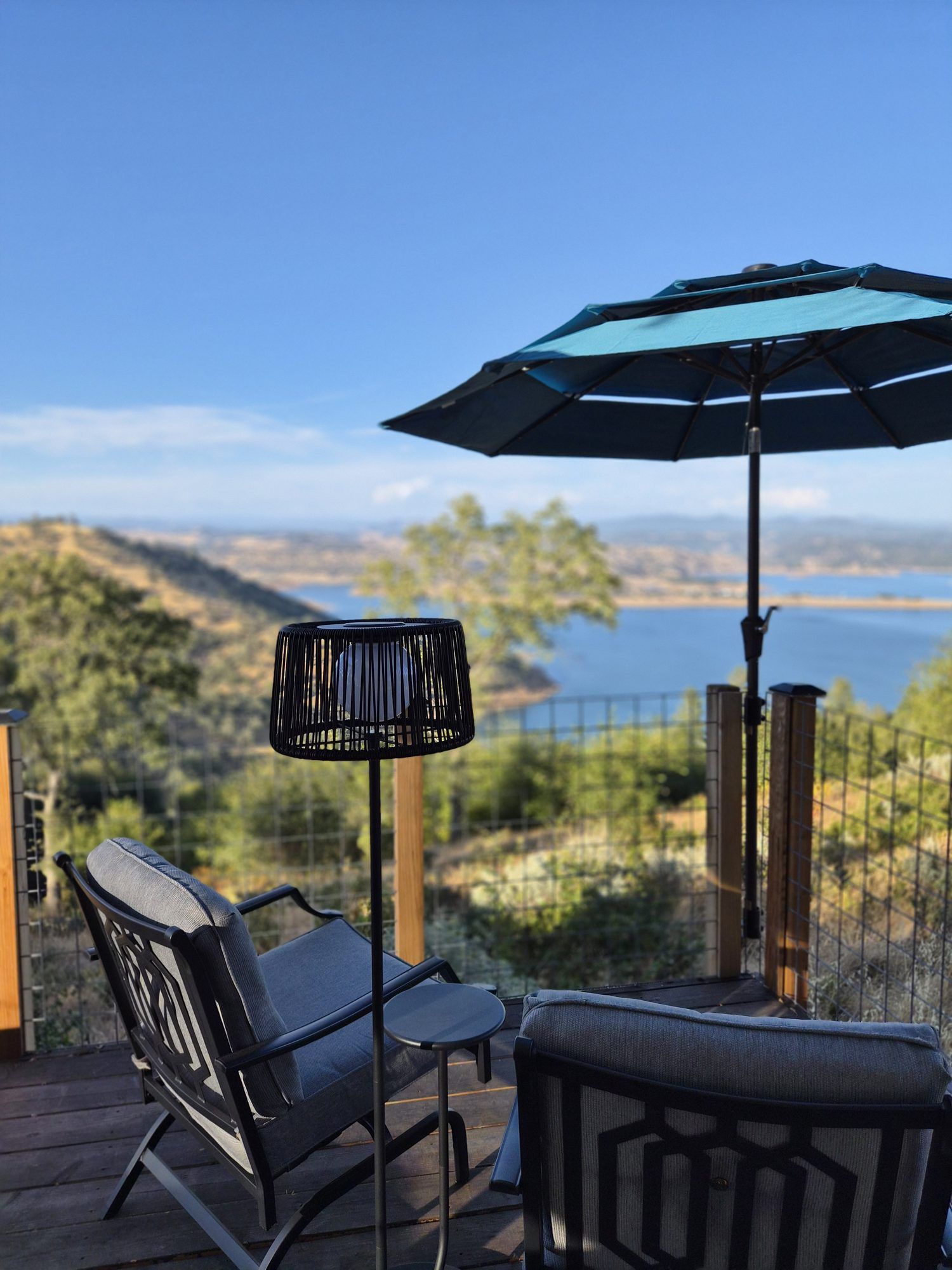 Una terraza con una silla, una mesa, una sombrilla y vistas a un lago y colinas.