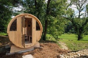 Una construcció de fusta circular amb una porta i finestres, situada en un entorn natural ple d'arbres i gespa.