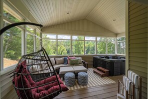 A sunroom with a hanging chair, a sofa with cushions, a hot tub, and a view of the outdoors. - Wanderwood | Sleeps 20 | 20 Acres + Pool + Golf (Laurelville)