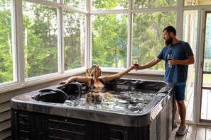 A hot tub with a person and another person outside the window. - Wanderwood | Sleeps 20 | 20 Acres + Pool + Golf (Laurelville)