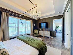 Une chambre à coucher avec un grand lit, un lustre, une télévision et une vue sur l’extérieur.