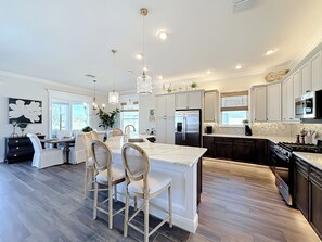 A modern kitchen with a central island, dark wood cabinets, stainless steel appliances, and pendant lighting. - Luxury Golf Front Retreat with Cascading Private Pool/Spa/Golf Cart (The Villages)