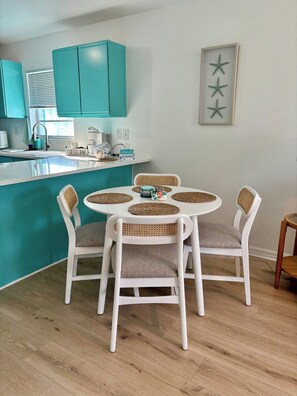 Un coin repas avec une table ronde, quatre chaises, un espace cuisine avec des meubles de couleur turquoise et une décoration en forme d’étoile fixée au mur.