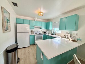 Une cuisine avec des armoires de couleur turquoise, un réfrigérateur blanc, une cuisinière et un four à micro-ondes.