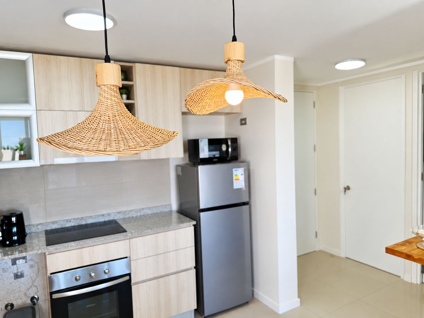 A modern kitchen with stainless steel appliances, light wood cabinetry, and two woven pendant lights.