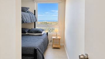 A bedroom with a bunk bed, a bedside table with a lamp, and a view of the landscape through a window.