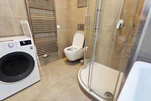 A compact bathroom with a washing machine, toilet, and glass-enclosed shower. - New Town Feel-at-Home Studio (Prague)