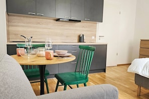 Eine moderne Küche mit grauen Schränken, einer Holz Arbeitsplatte und einem Essbereich mit rundem Tisch und grünen Stühlen.