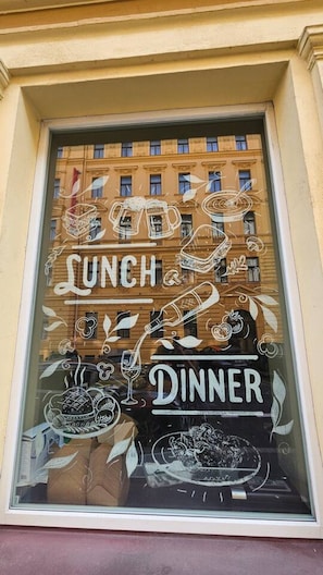 Ein Restaurantfenster mit Dekorationen und der Aufschrift 'LUNCH' und 'DINNER', die die Art der angebotenen Mahlzeiten kennzeichnet.