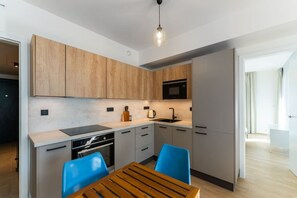 A modern kitchen with wooden cabinets, a black stove, and a blue chair. - New  build Distillery Apartment by Rentez (Prague)
