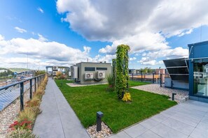 A modern building with outdoor air conditioning units, a grassy area, and a paved walkway. - New  build Distillery Apartment by Rentez (Prague)