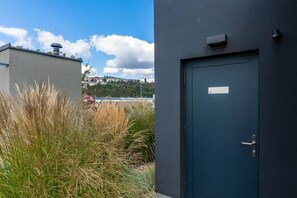 Edifici amb una porta blau fosc i un rètol, envoltat d'herba alta i un cel clar.