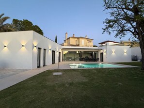 Ein modernes Haus mit einem Swimmingpool, einer überdachten Terrasse und einem großen Fenster mit Blick auf den Pool.