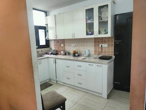 Cozinha com armários brancos, bancada com diversos eletrodomésticos e painel de azulejos.