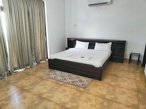 Quarto com cama, mesa de cabeceira, pequena mesa e ar-condicionado fixado na parede.