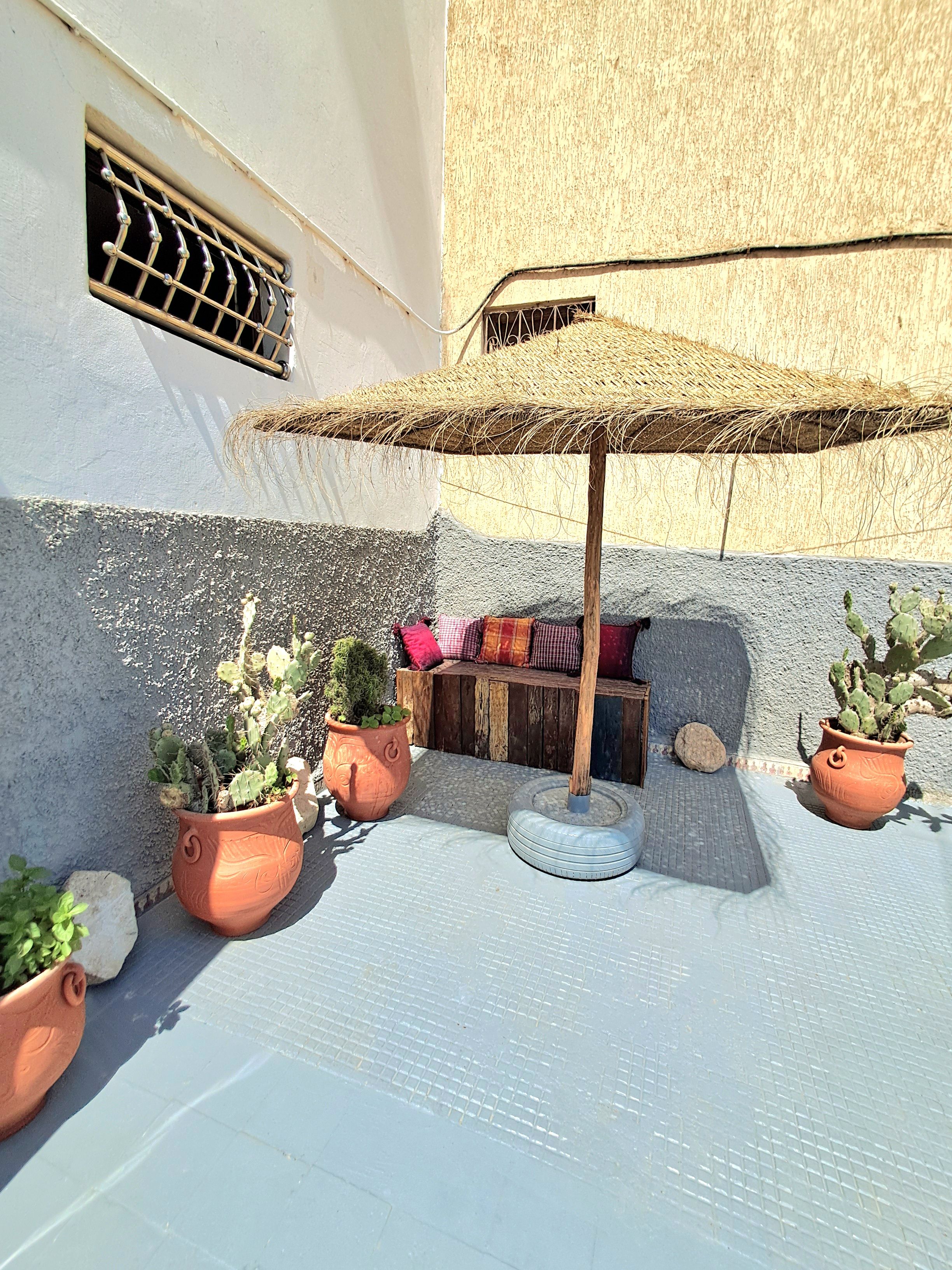 A courtyard with potted plants, a wooden bench, and a thatched umbrella.