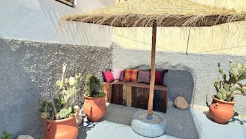 A courtyard with potted plants, a wooden bench, and a thatched umbrella.