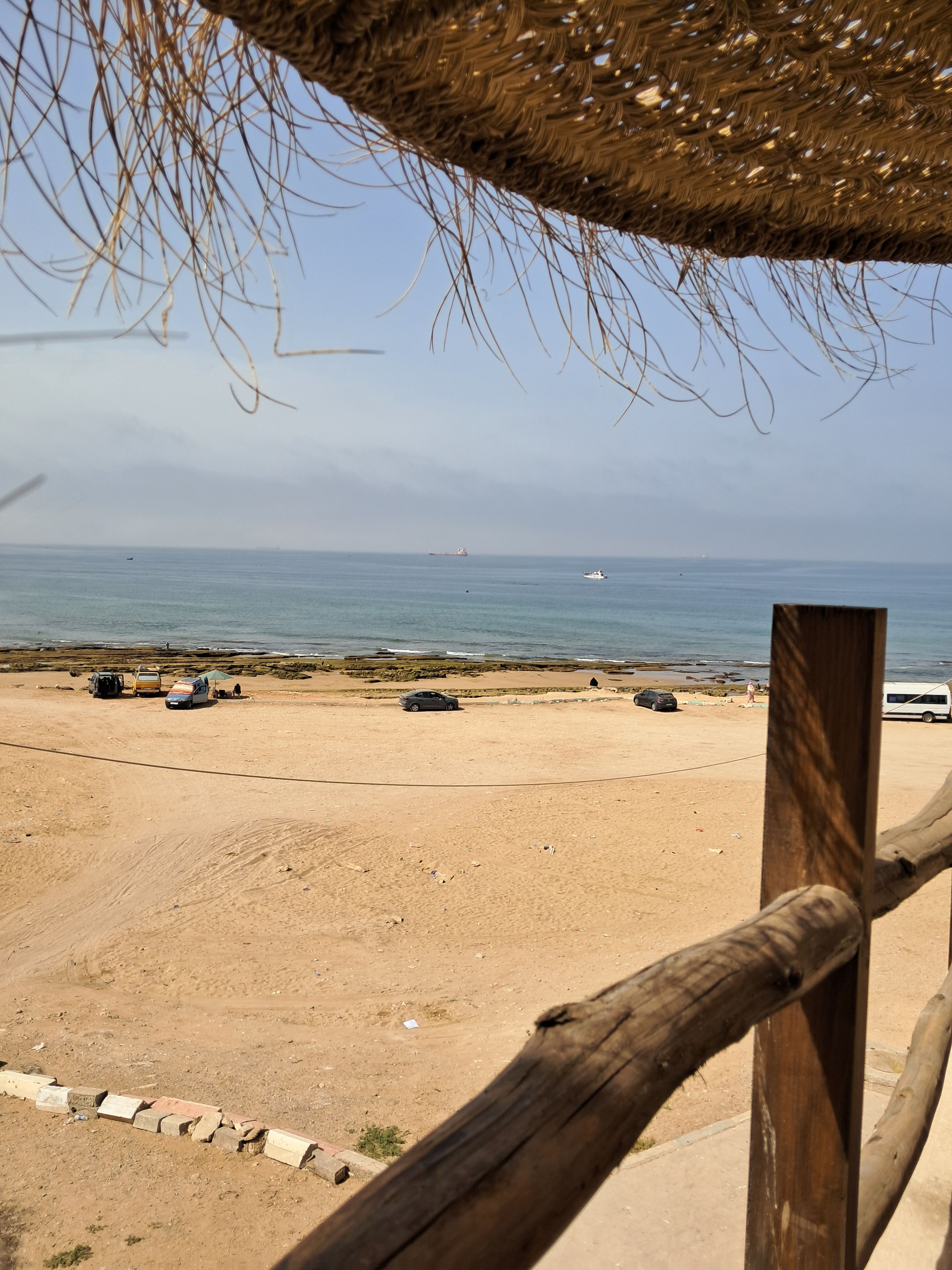 A beach with a thatched roof structure, a sandy shore, and a view of the sea.