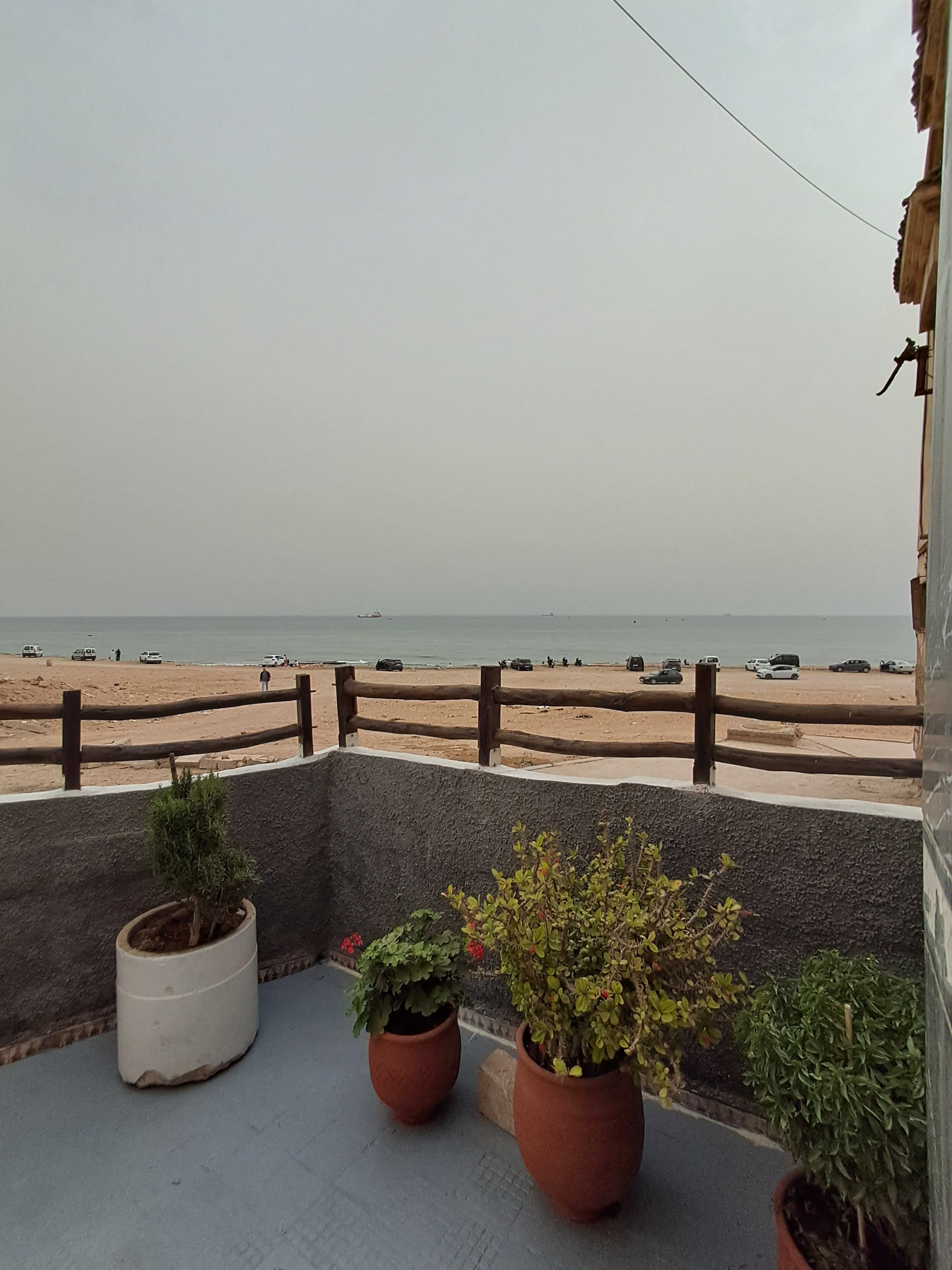 A balcony with potted plants overlooking a beach with a wooden fence.