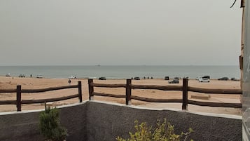 A balcony with potted plants overlooking a beach with a wooden fence.