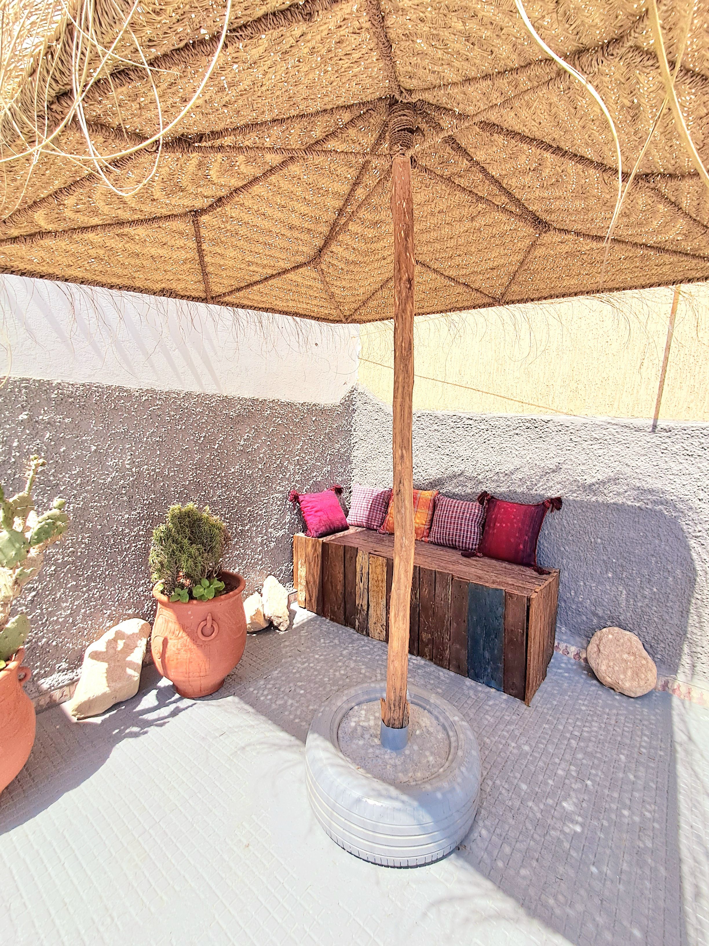 A seating area with a wooden bench, a potted plant, and a large umbrella.