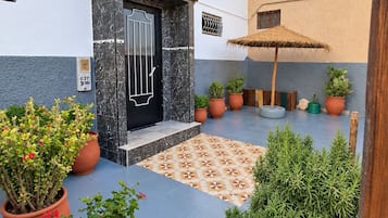 A courtyard with a tiled floor, potted plants, a door with a metal gate, and a small umbrella.