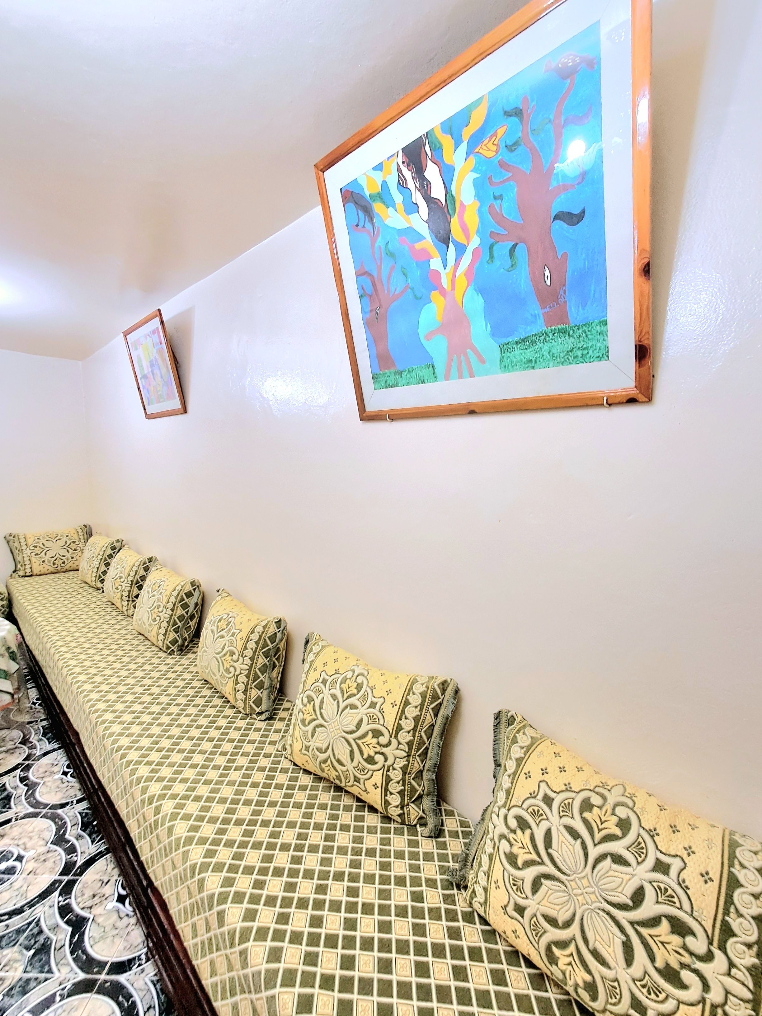 A room with a long sofa against a wall, a framed picture above it, and patterned floor tiles.