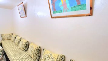 A room with a long sofa against a wall, a framed picture above it, and patterned floor tiles.