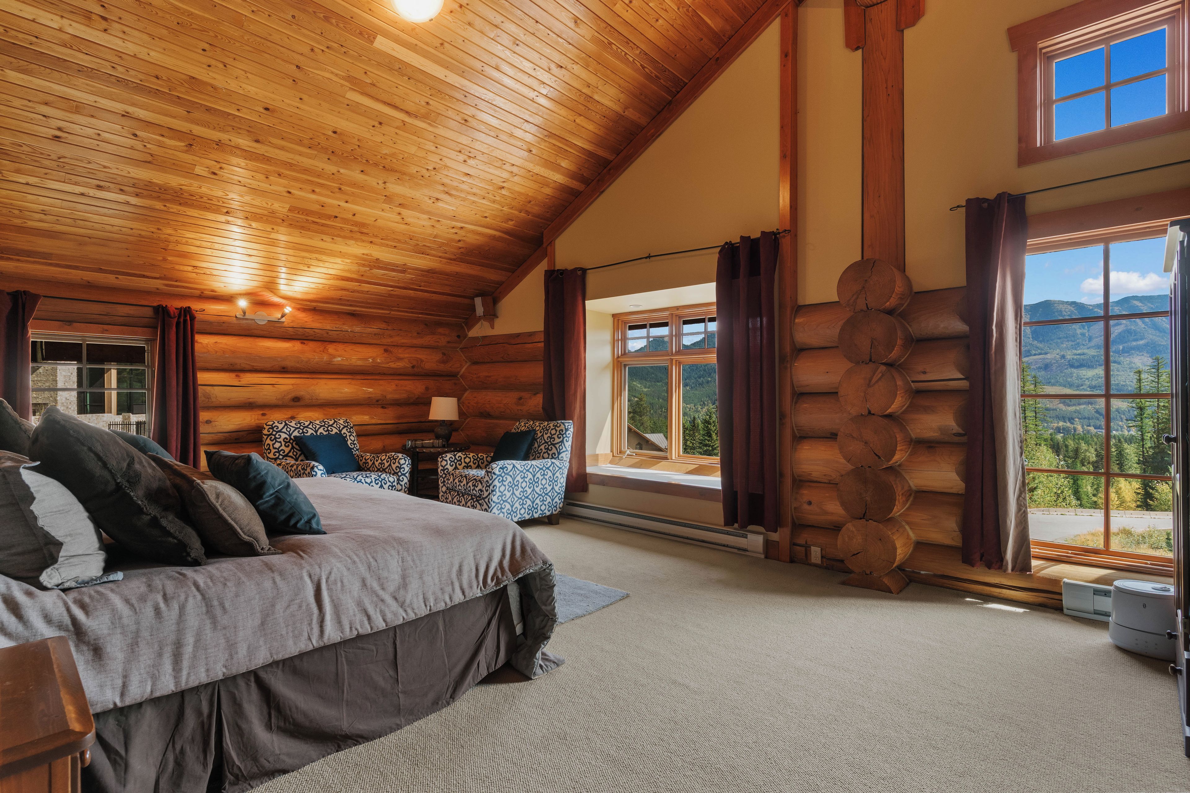 A log cabin bedroom with a bed, chairs, a table, and a large window with a view of mountains.