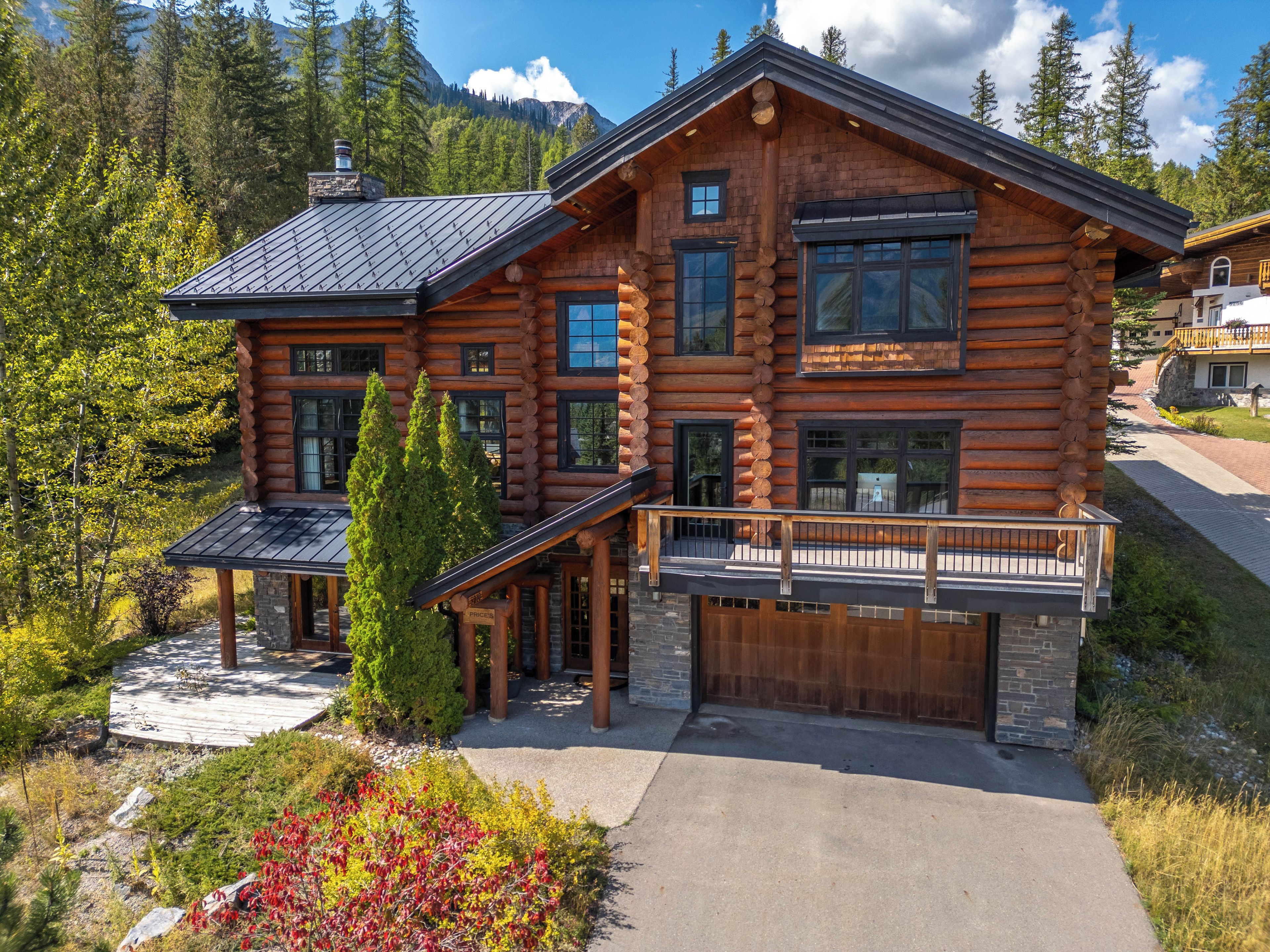 A log cabin with a large deck, multiple windows, and a garage.