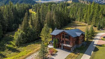 A cabin with a porch, surrounded by dense forest and mountains in the background.