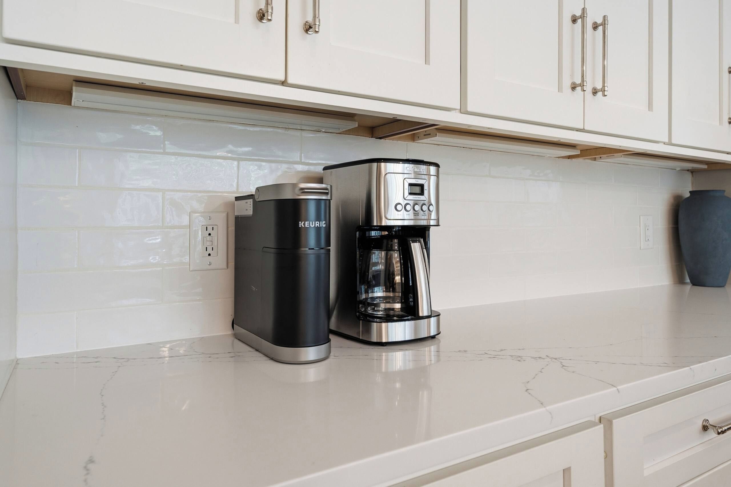 Eine moderne Küche mit weißen Schränken, einer Kaffeemaschine und einem Wasserkocher auf einer Marmorarbeitsplatte.