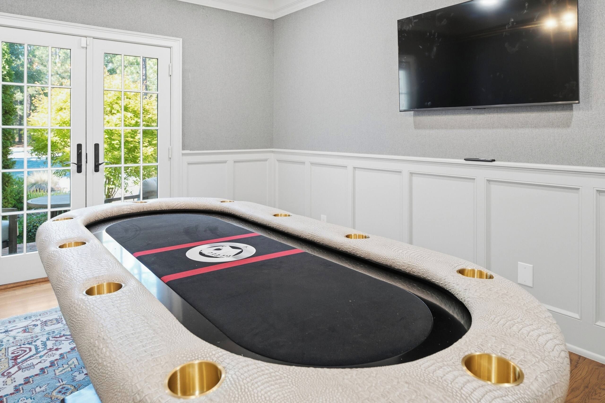 A pool table with a unique design, a television mounted on the wall, and a view of greenery outside.