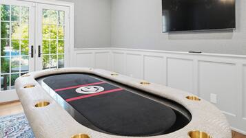 A pool table with a unique design, a television mounted on the wall, and a view of greenery outside.