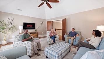 Ein Wohnzimmer mit Fernseher, auf dem 'NETFLIX' angezeigt wird, einem Deckenventilator und einer Tür zu einem anderen Raum.