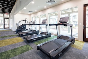 Et fitnesscenter med løbebånd, et vægmonteret display og et tæppe.