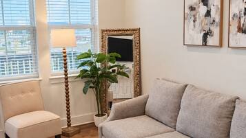 A living room with a beige sofa, a chair, a floor lamp, a potted plant, and two abstract paintings on the wall.