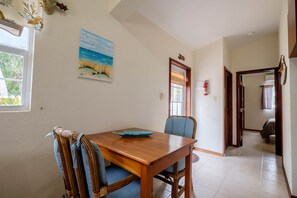 A dining area with a wooden table and chairs, a painting on the wall, and a door with a sign. - Oceanfront Casita w/pool-kayaks-paddleboards-beach (San Pedro)